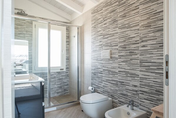 A modern bathroom with a glass shower enclosure, a toilet, and a sink. - Jasmin Penthouse Vacation Home (Quartu Sant'Elena)