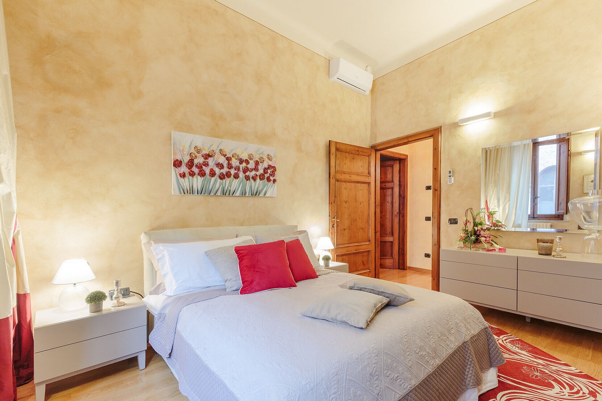 A bedroom with a bed, nightstands, a dresser, a mirror, and a painting on the wall.