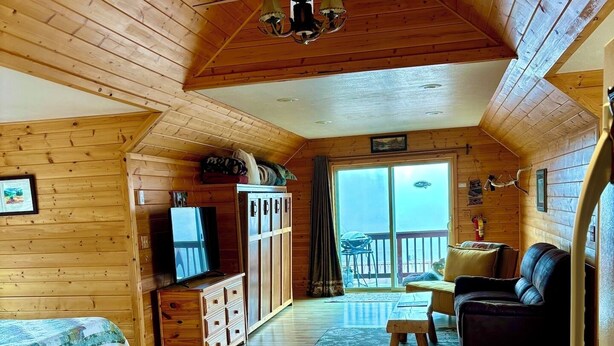 A cozy cabin interior with a wooden floor, a bed, a sofa, a dining table, and a ceiling fan.