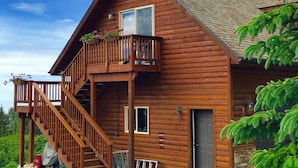 A wooden cabin with a balcony, a staircase, and a door.