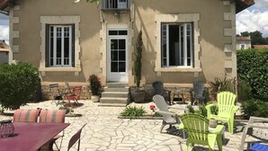 Ein zweistöckiges Haus mit Balkon, Eingangstür und einer Terrasse mit Gartenmöbeln.
