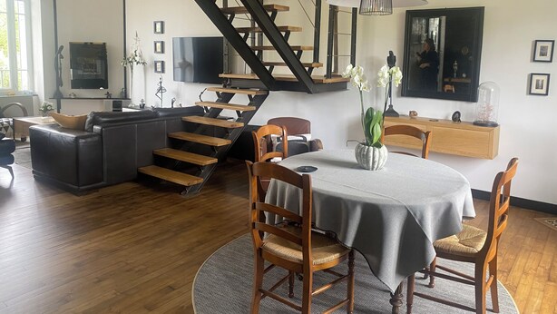 Ein modernes Wohnzimmer mit Treppe, einem Essbereich mit rundem Tisch und einer Küchenzeile.