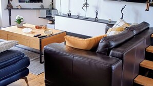 Ein modernes Wohnzimmer mit einer Ledersofa, einem Holztisch und einem flachbildfernseher an der Wand.