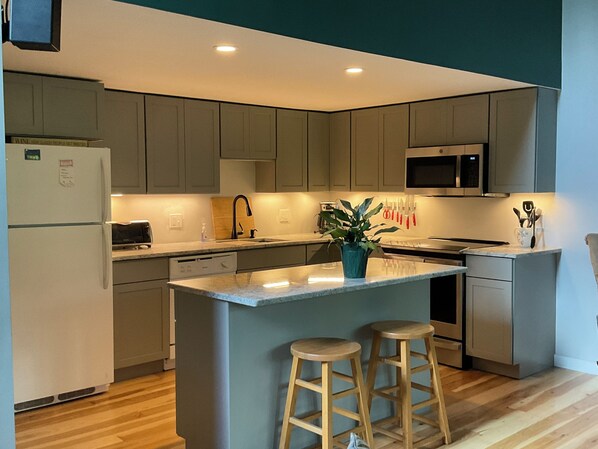 A modern kitchen with grey cabinets, a central island with stools, a microwave, and a refrigerator.