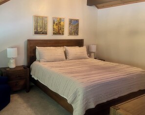 A bedroom with a wooden headboard, two bedside tables with lamps, a bed with a striped bedspread, and three framed pictures on the wall.