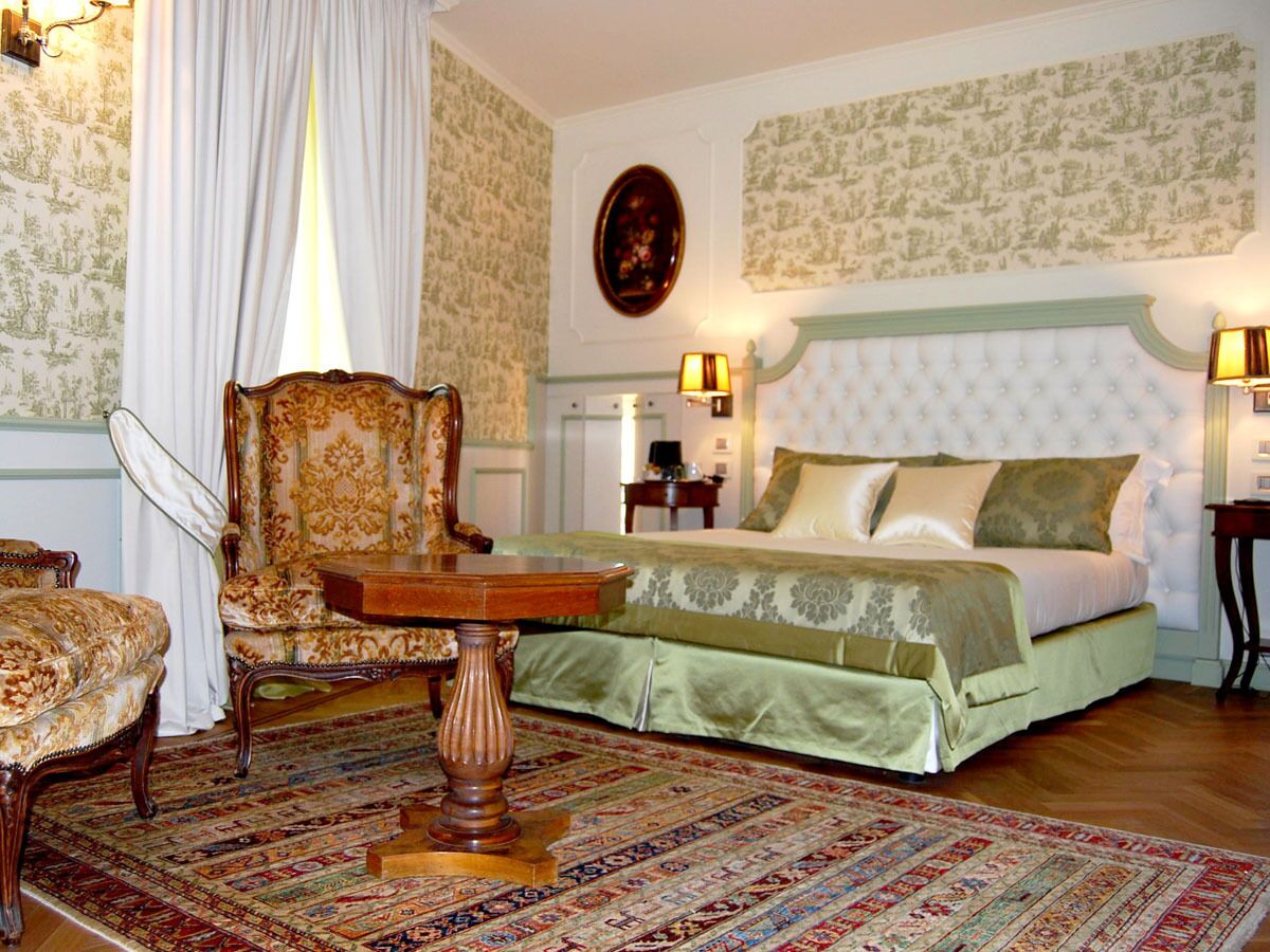 A traditional bedroom with a bed, a chair, a table, and a patterned rug.