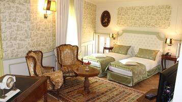 Habitación de hotel con dos camas, una zona de estar con mesa, un escritorio con teléfono y televisión.