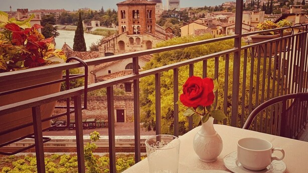 A balcony with a table set for tea, a slice of cake, and a red rose. - Relais Colle San Pietro (Verona)