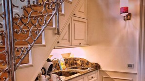 A kitchen with a wooden staircase, white cabinets, a marble countertop, and a dining area with a patterned tablecloth. - Relais Colle San Pietro (Verona)
