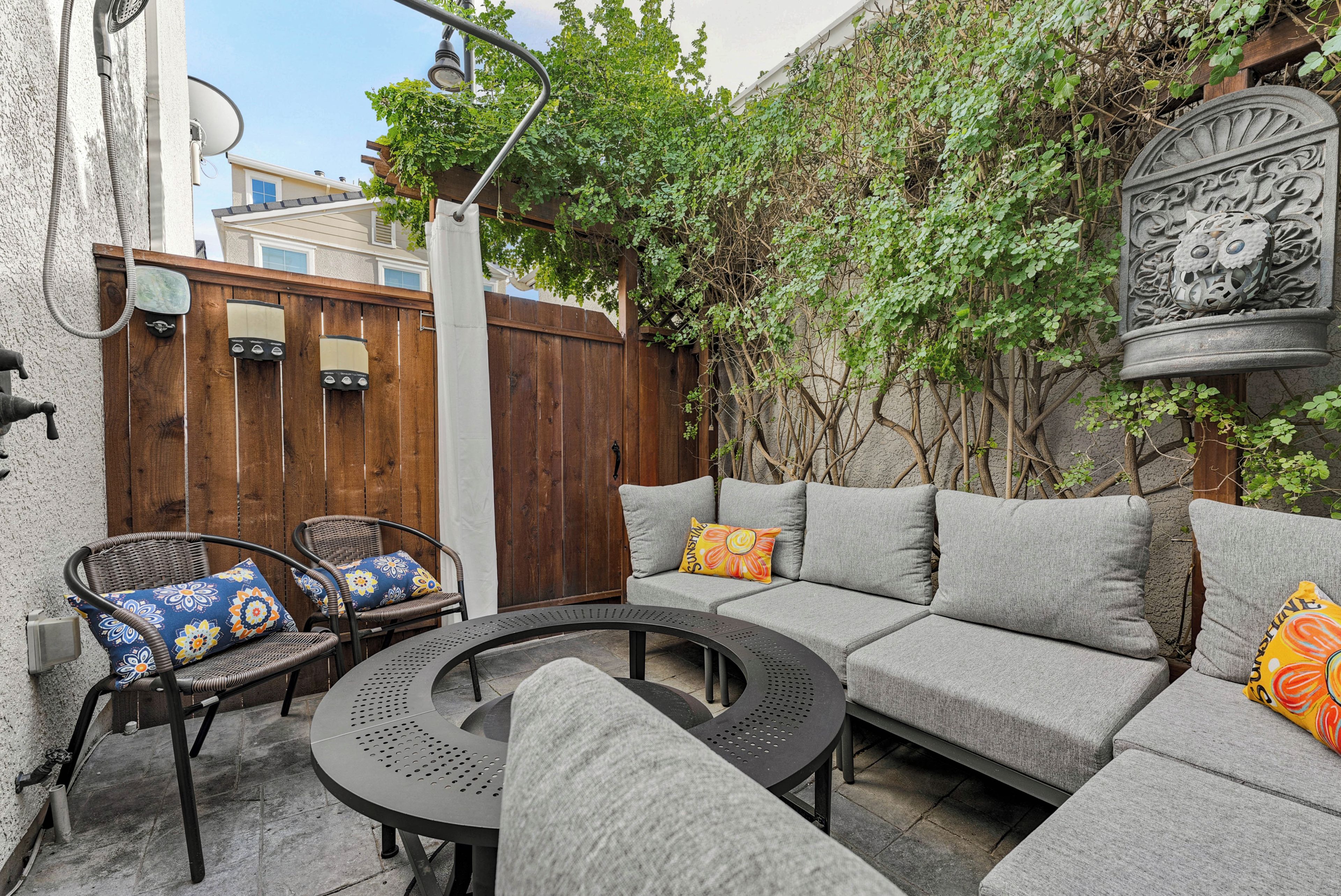 Une terrasse avec une table ronde, deux chaises en osier, un canapé gris et une clôture en bois.
