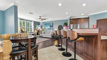 A modern kitchen with wooden cabinets, a bar area with stools, and a dining table with chess set.