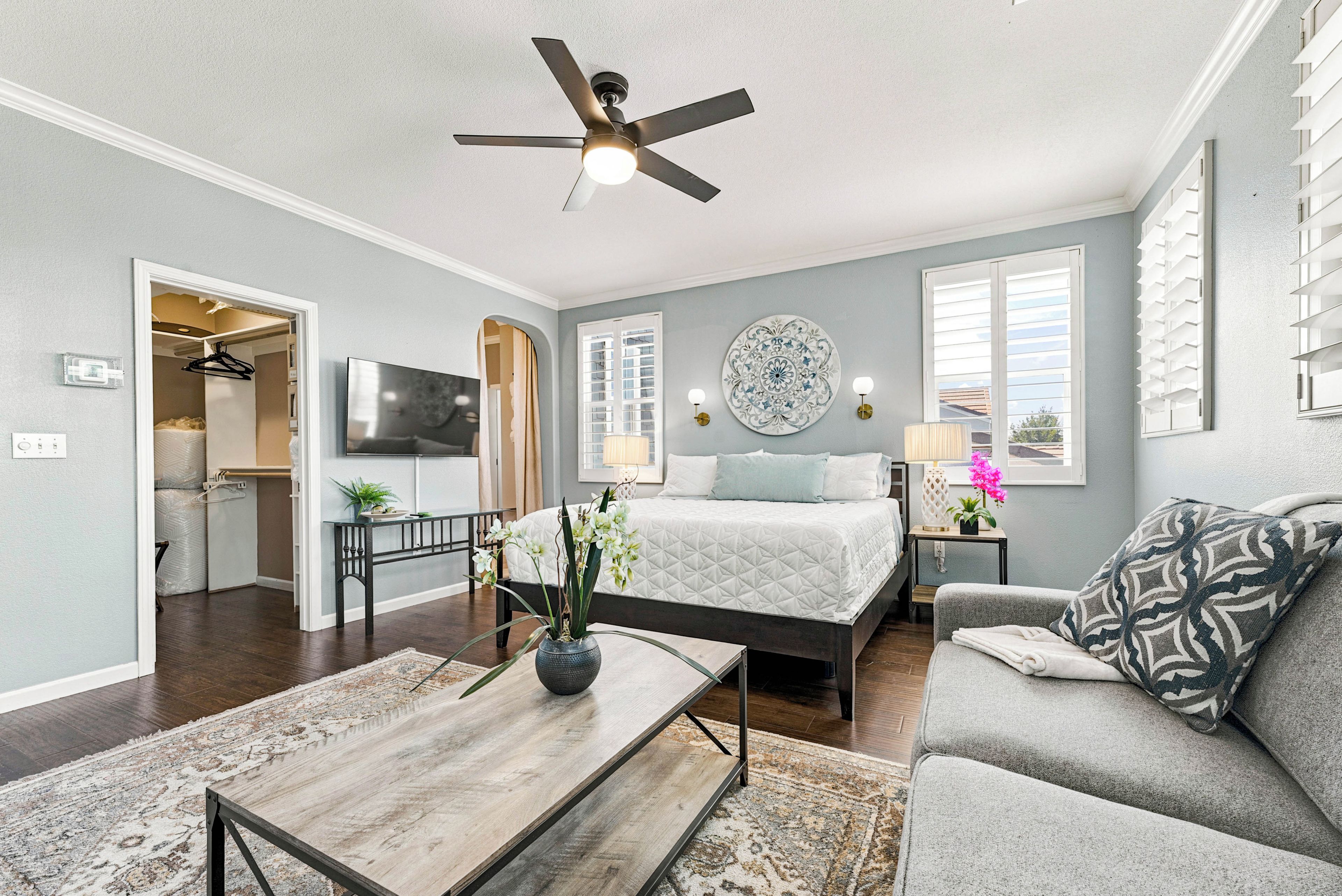 A modern bedroom with a bed, a ceiling fan, a TV, and a view of the outside.