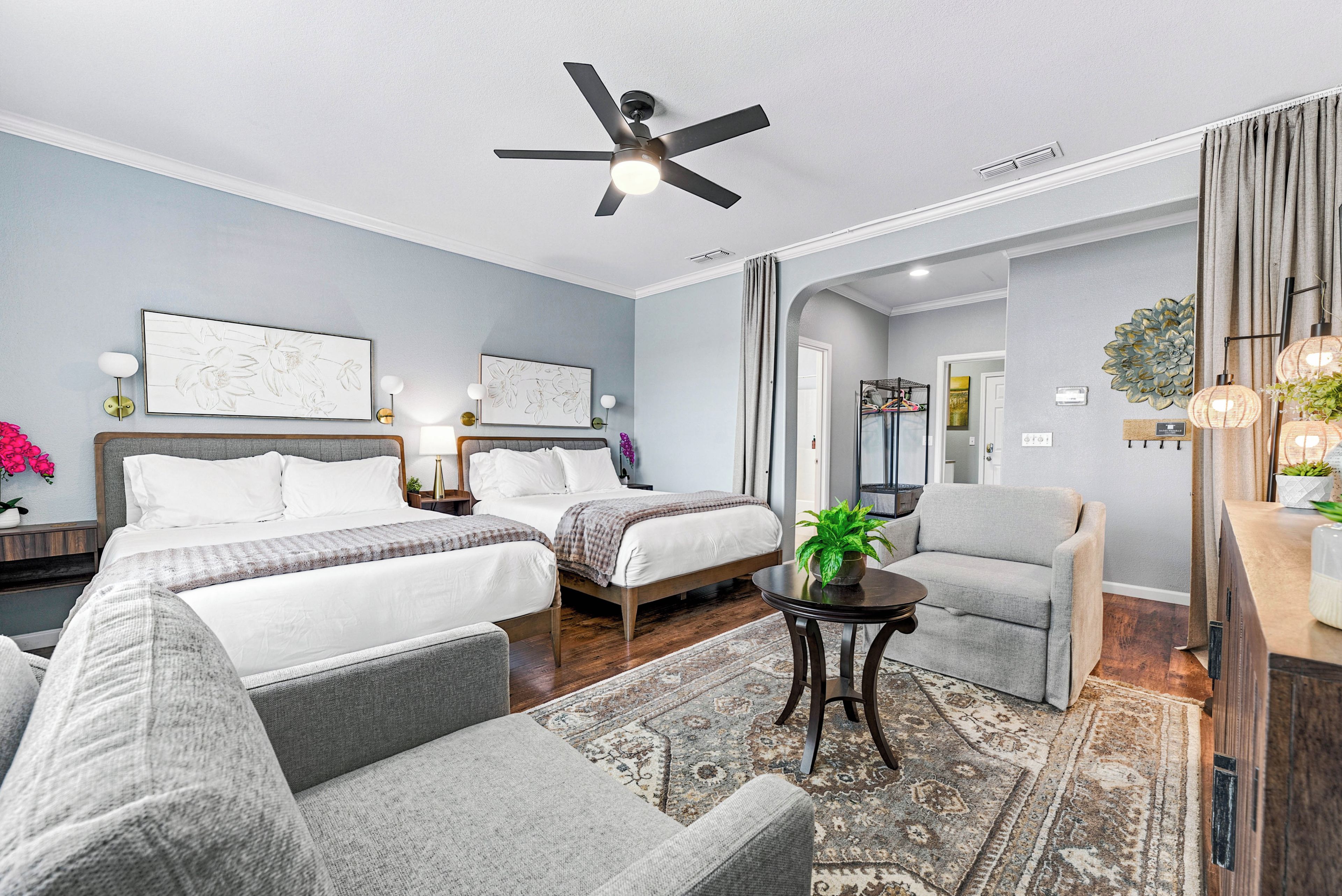 A hotel room with two beds, a chair, a small table, and a ceiling fan.