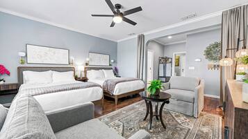 A hotel room with two beds, a chair, a small table, and a ceiling fan.