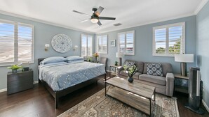 A bedroom with a bed, a ceiling fan, a nightstand, a dresser, a window, and a nightstand lamp.