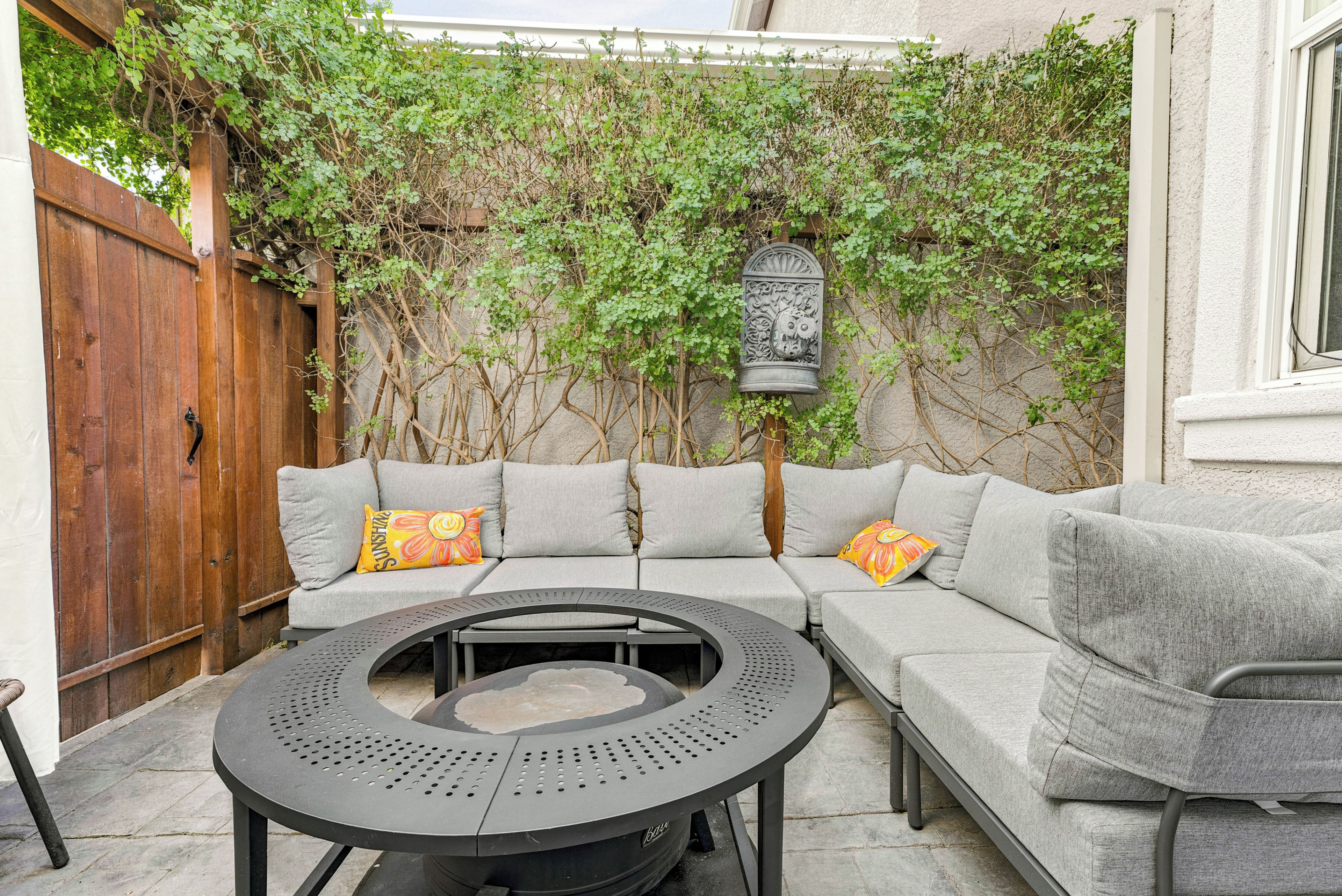 A patio with a round table, grey cushioned seating, and a wooden fence.