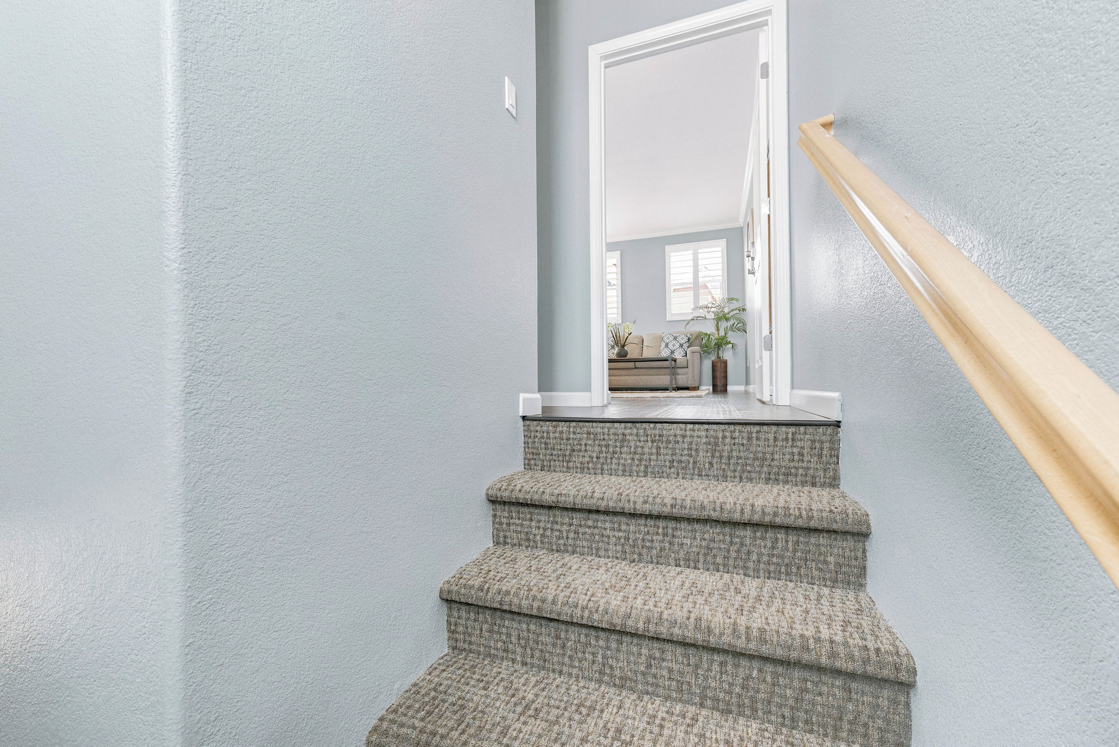Un escalier recouvert d’une moquette à motifs et doté d’une rampe en bois, menant à une porte.