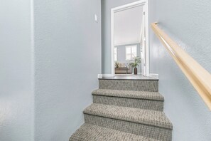 Una escalera con alfombra texturizada y barandilla de madera que lleva a una puerta.