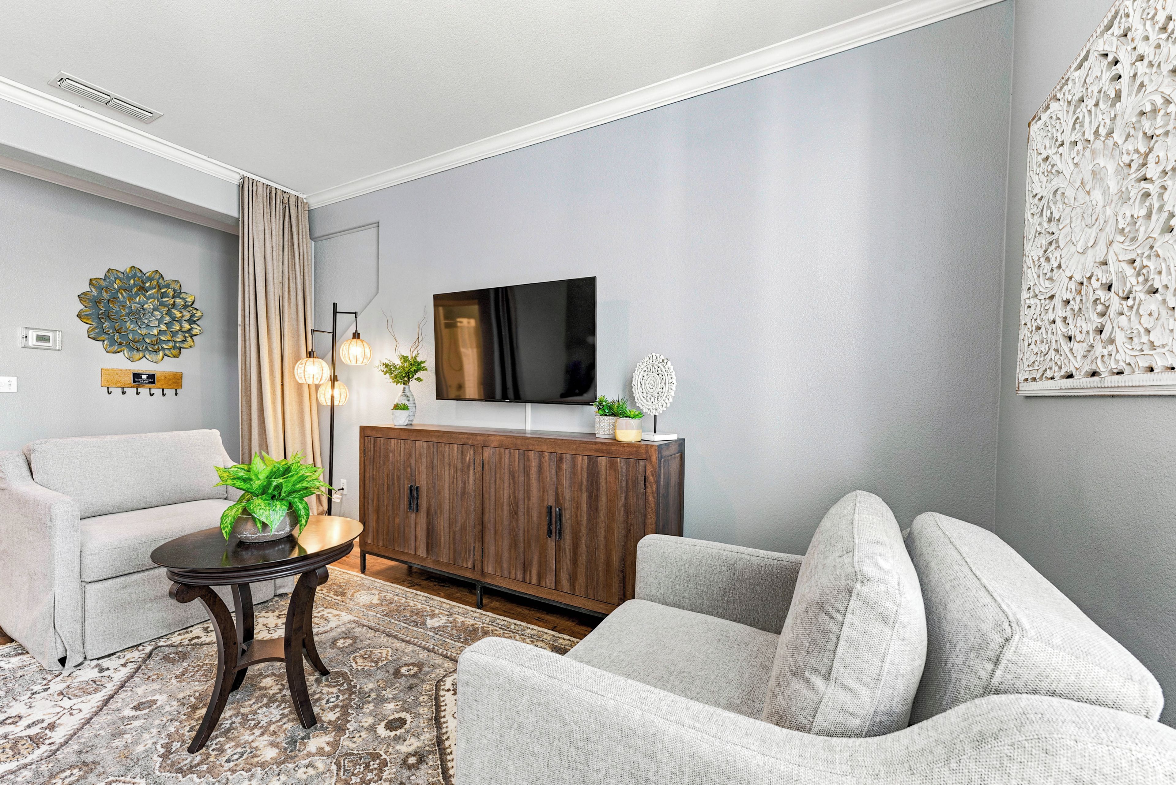 Uma sala de estar moderna com sofá, poltrona, televisão, painel decorativo e um armário.