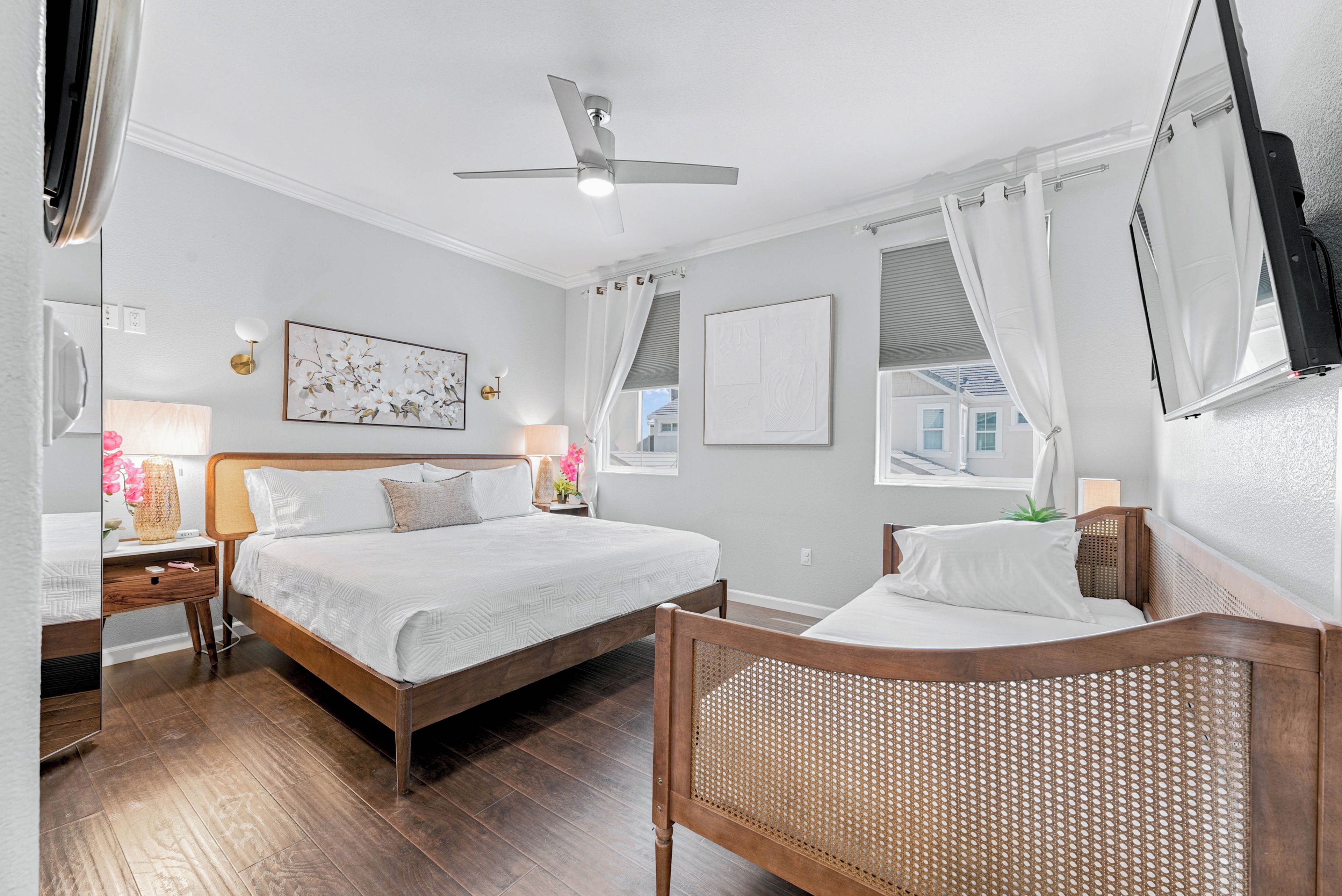 Une chambre d’hôtel avec un lit, une chaise, un ventilateur de plafond et des œuvres d’art accrochées aux murs.