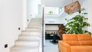 Una escalera que lleva a un balcón, una zona de cocina y un sofá.