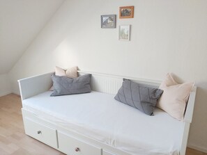 Ein niedriges Bett in Weiß mit Stauraumschublade und zwei Kissen.