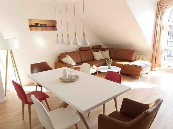 Ein modernes Wohnzimmer mit einem weißen Esstisch, einem braunen Ledersofa und roten Stühlen.