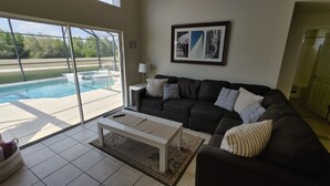 A living room with a black sofa, a white coffee table, and a pool view through glass doors. - Spectacular Lake View - Game/Media Room - Vacation Home Close to Disney (Kissimmee)