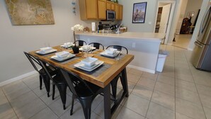 A modern kitchen with wooden cabinets, a stainless steel refrigerator, and a dining area with a wooden table set for four. - Spectacular Lake View - Game/Media Room - Vacation Home Close to Disney (Kissimmee)