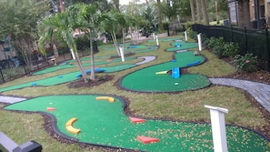 Un campo da minigolf con diverse buche, circondato da una recinzione e palme.