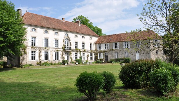 Een groot, historisch gebouw met een symmetrische gevel, meerdere ramen en een verzorgd gazon ervoor.