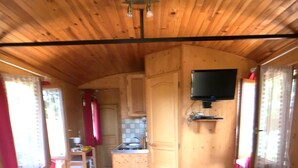 Een gezellig interieur van een chalet met houten vloeren, een kitchenette, een aan de muur bevestigde televisie en twee bedden met rode beddengoed.