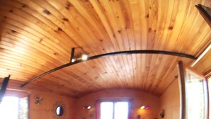 Een gezellig blokhutinterieur met houten vloeren en wanden, een zithoek, een klein tafeltje en een raam.