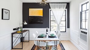 A dining area with a white table set for two, a black and yellow abstract painting above, and a window with white curtains. - Sun filled + Airy Large 2 Bedroom apt in West adam’s (Los Angeles)