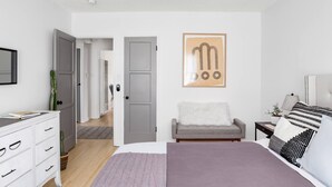 A bedroom with a bed, a nightstand, a chair, a dresser, a ceiling fan, and a door. - Sun filled + Airy Large 2 Bedroom apt in West adam’s (Los Angeles)