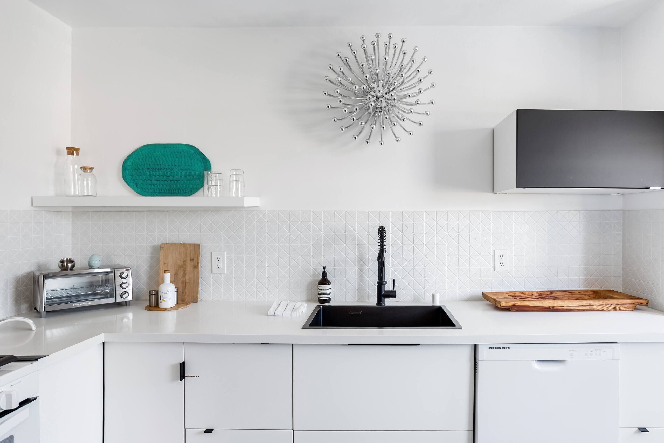 Een moderne keuken met witte kasten, een ingebouwde toaster, een zwarte spoelbak en een houten snijplank.
