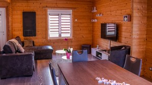 L’intérieur chaleureux d’un chalet, avec un décor en bois, une table à manger, des canapés, un téléviseur et une fenêtre avec des volets.