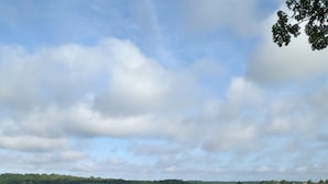 Une terrasse en bois, dotée de bancs et d’un foyer extérieur, qui offre une vue sur un paysage verdoyant avec des maisons visibles au loin.