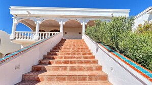 Eine Treppe mit roten Fliesen führt zu einem weißen Gebäude mit Bögen und einem Balkon.