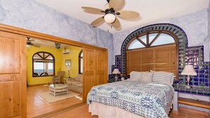 Ein Schlafzimmer mit einem Bett, einem Deckenventilator, einem Fenster mit Holzjalousien und einer gefliesten Wand.