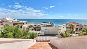 Ein Küstenwohngebiet mit freiem Blick auf das Meer, ein weißes Gebäude mit rotem Ziegeldach und eine Treppe, die zu einer höheren Ebene führt.