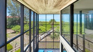 A room with large windows offering a view of a beach and greenery.