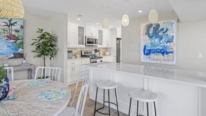 A modern kitchen with white cabinets, a central island with stools, pendant lights, and a large framed artwork on the wall.