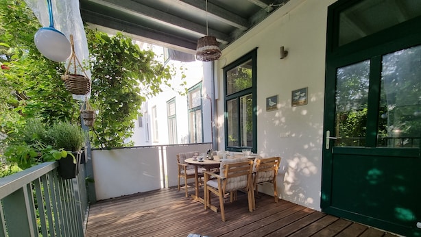 A wooden deck with a table and chairs, a hanging light fixture, and a green door. - Modern apartment with large balcony 110m² / free garage with e-charging station (Wien)