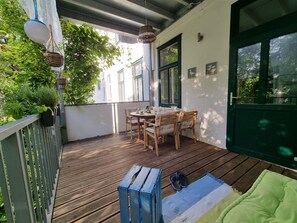 Una terraza de madera con una mesa y sillas, una lámpara colgante y una puerta verde.