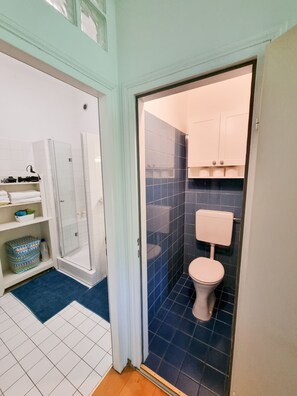 Un baño con ducha, inodoro y estantes de almacenamiento.
