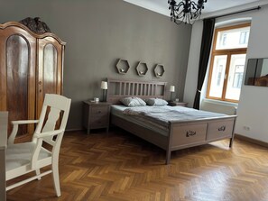 A bedroom with a wooden bed, a nightstand, a dresser, a chair, and a window with curtains.