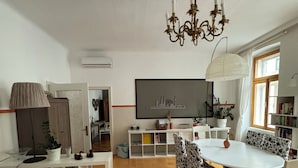 A spacious living room with a dining area, a chandelier, a large flat-screen TV, and a bookshelf. - Modern apartment with large balcony 110m² / free garage with e-charging station (Wien)