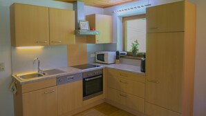A compact kitchen with wooden cabinets, a built-in microwave, a dishwasher, and a window with a view. - 110m² vacation apartment in a quiet location in the wild and romantic Zillertal valley (Mayrhofen)