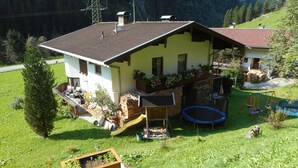 A house with a sloped roof, a balcony with plants, a trampoline, and a wooden playhouse. - 110m² vacation apartment in a quiet location in the wild and romantic Zillertal valley (Mayrhofen)